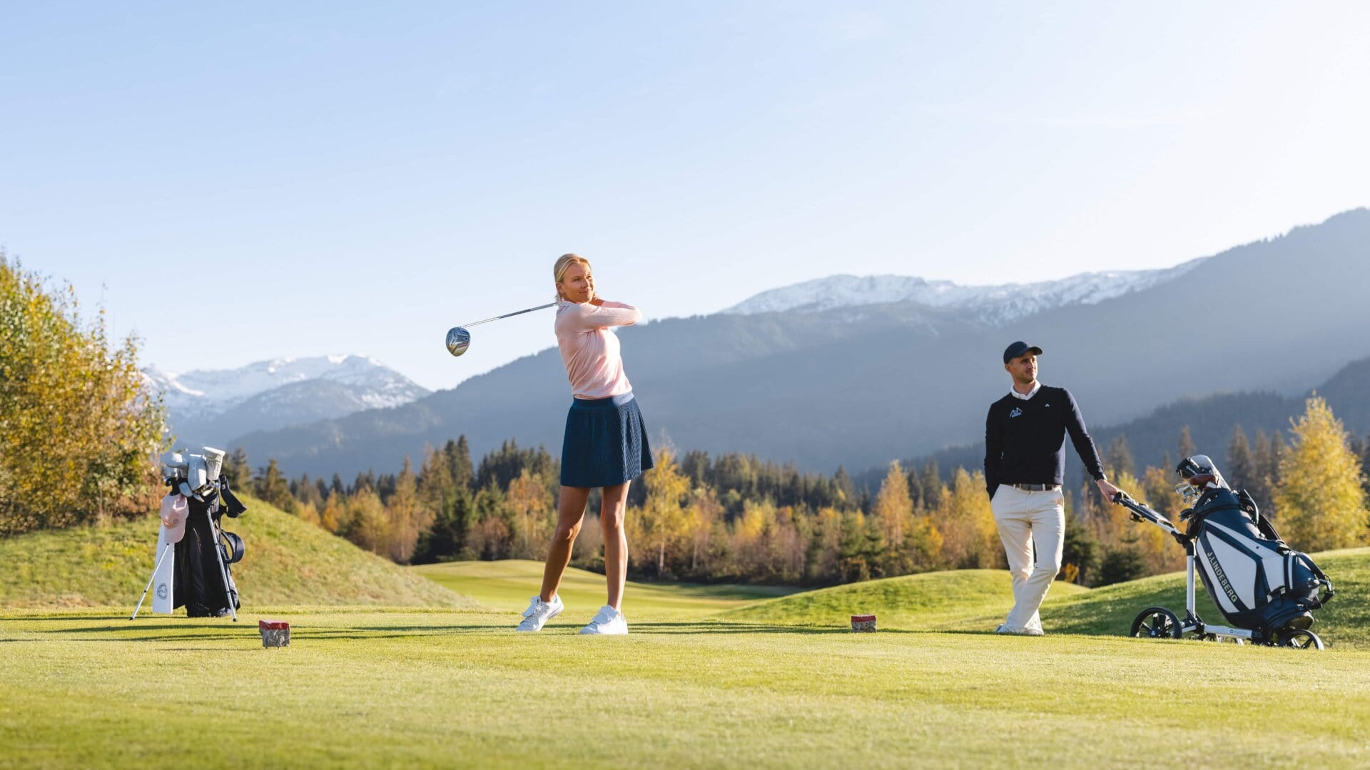 Golferin schlägt auf einem Platz mit Bergen zu.