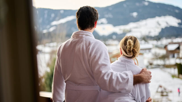 Paar in Bademänteln auf Balkon mit Bergblick